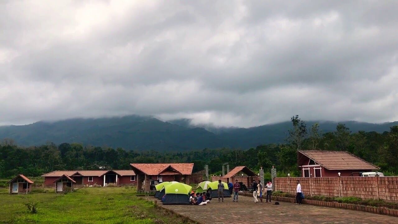 A series of rustic cabins with red roofs, set against a backdrop of mountains and cloudy skies.