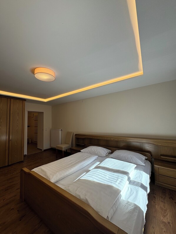 A bedroom with a wooden bed, bedside tables, a chair, and a wardrobe. - Hotel Goldenes Kreuz (Vipiteno)