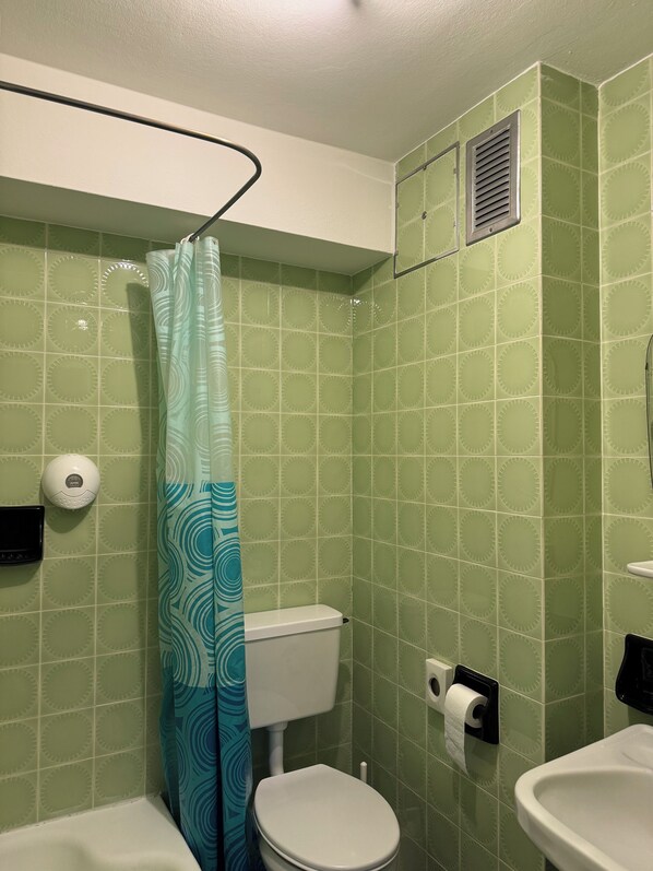 A bathroom with green patterned tiles, a toilet, a sink, a shower curtain, and a hand dryer. - Hotel Goldenes Kreuz (Vipiteno)