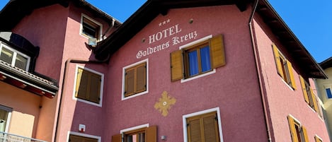 Un edificio rosa con el letrero "HOTEL Goldenes Kreuz" y un balcón con barandilla de madera.