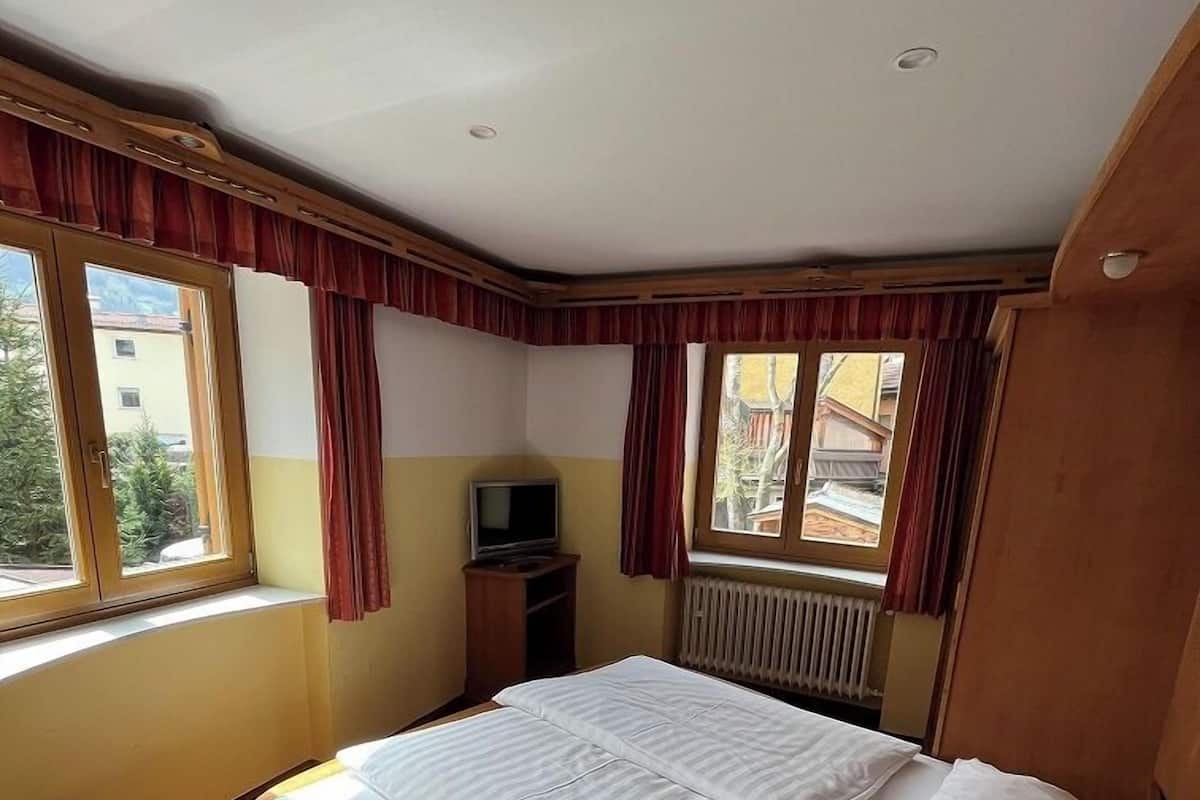 A bedroom with a wooden bed, a television, and windows with curtains.