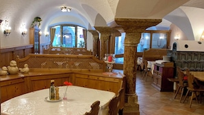 A dining area with a round table, wooden chairs, and a stone pillar. - Hotel Goldenes Kreuz (Vipiteno)