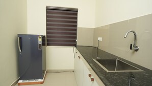 Μια μικρή κουζίνα με ψυγείο, νεροχύτη και ένα παράθυρο με περσίδες.