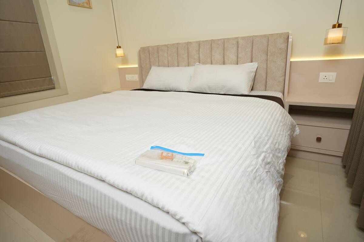 A neatly made bed with white linens, a headboard, and bedside tables with lamps.