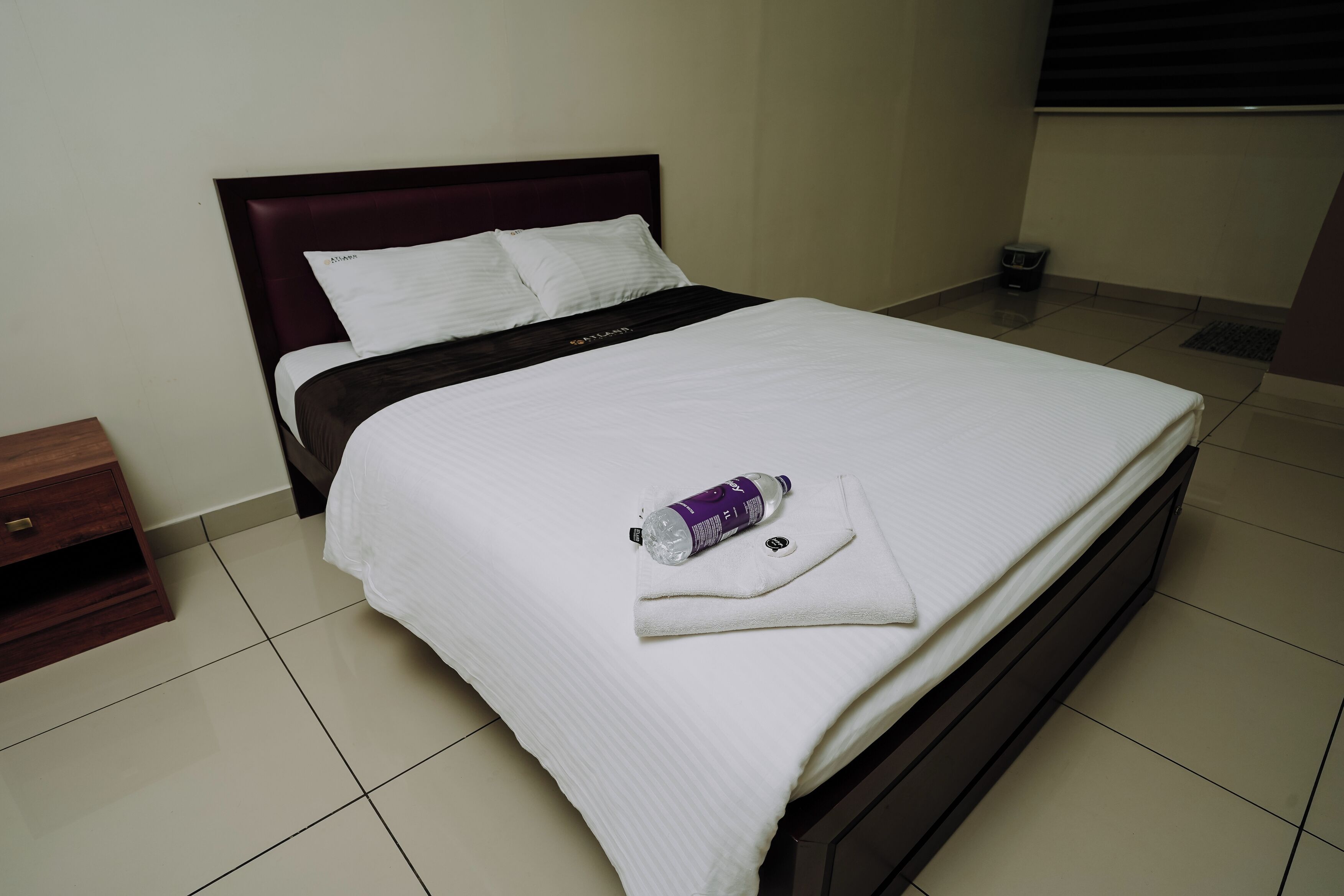 A neatly made bed with white bedding and a purple water bottle on it.