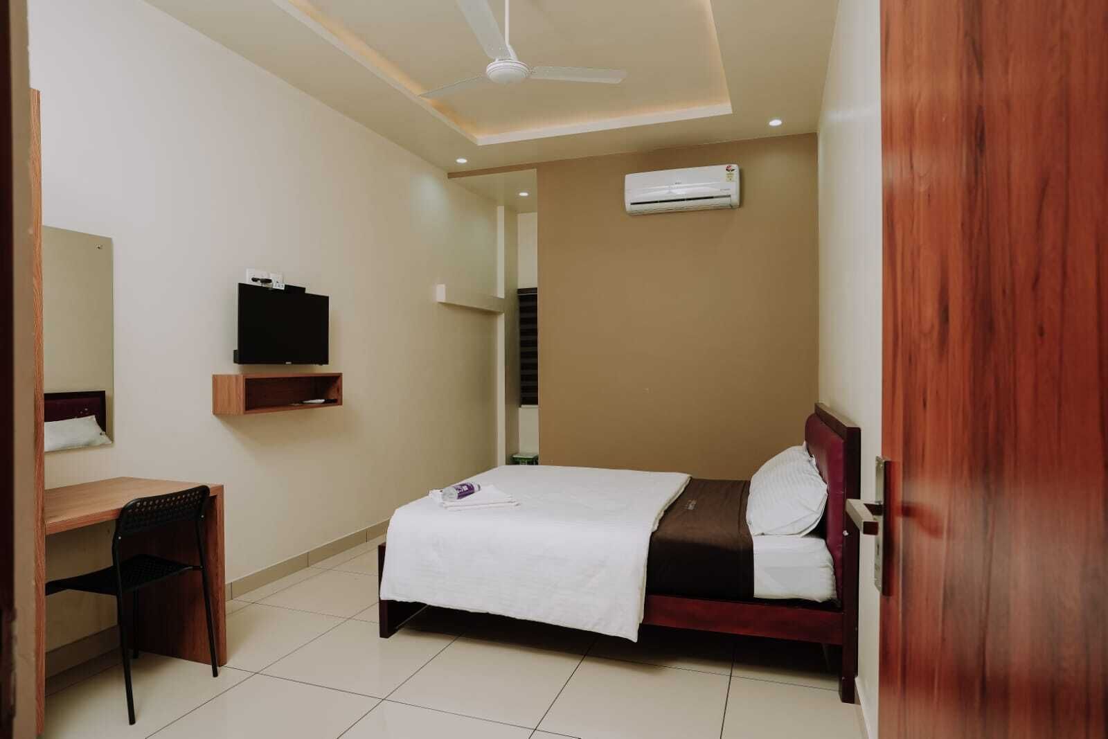 Una habitación de hotel con cama, escritorio, silla, televisor y aire acondicionado.