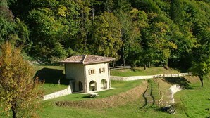 Een gebouw van steen met een pannendak, omringd door gras en bomen.