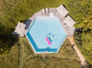 Eine Vogelperspektive eines sechseckigen Schwimmbeckens mit Holzterrasse, umgeben von üppiger Vegetation.