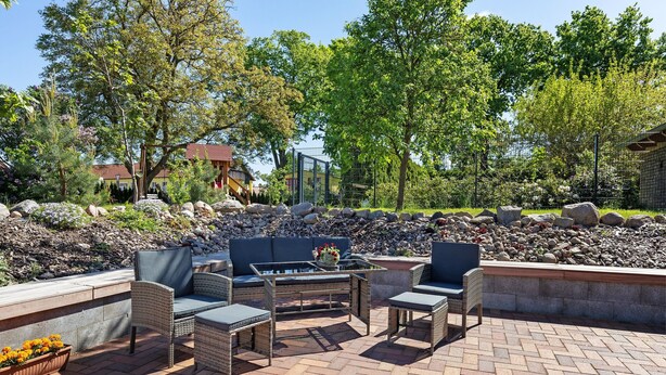 An outdoor patio with wicker furniture, a fire pit, and a view of a building with a red roof.
