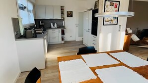 Eine moderne Küche mit weißen Schränken, ein Essbereich mit Holztisch und ein Wohnbereich mit einer Couch.