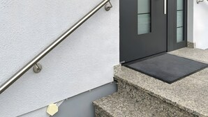 Ein moderner Eingangsbereich mit Glastür, Metallgeländer und einer kleinen Außenfläche mit Fußmatte.