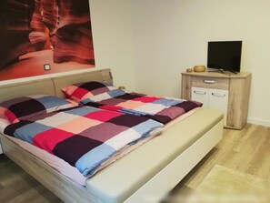 A bedroom with a bed, a wooden nightstand with a TV, and a large poster on the wall. - Apartment 'Am Silberg' with Mountain View, Private Terrace, and Wi-Fi (Plettenberg)