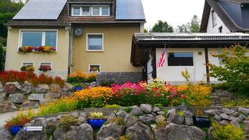 Zwei Häuser mit Solaranlagen, einer Steinmauer und bunten Blumenbeeten.