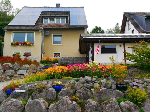 Dos casas con paneles solares, un muro de piedra y coloridos jardines de flores.