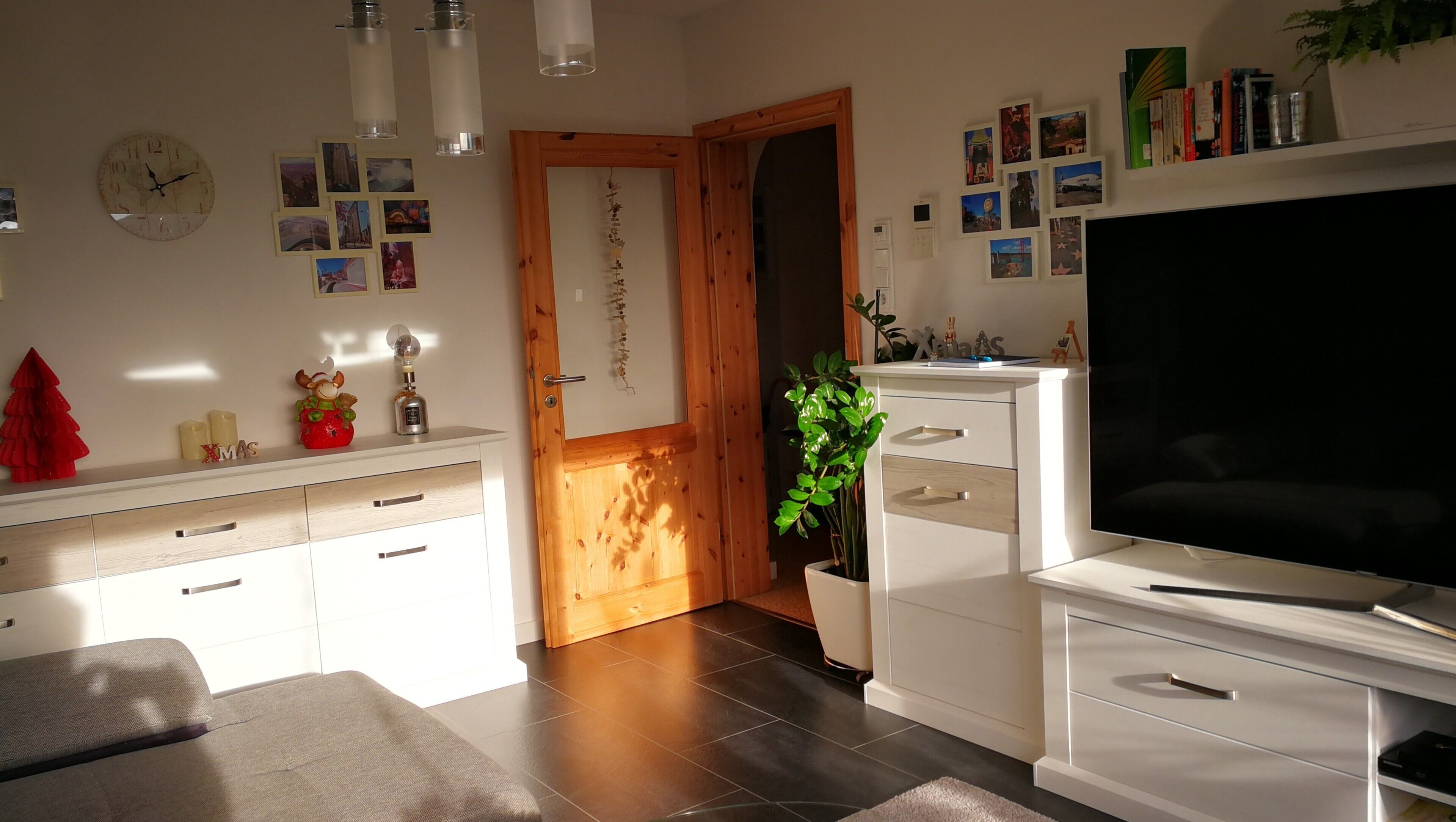 Een moderne woonkamer met een grote flatscreen televisie, een houten deur en een potplant.