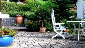 Un espace patio avec un sol en briques, une chaise blanche, une table et des plantes en pot.