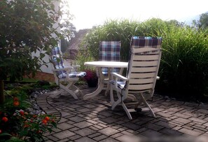 A patio with a table and two chairs, surrounded by greenery and a brick pathway. - Apartment 'Am Silberg' with Mountain View, Private Terrace, and Wi-Fi (Plettenberg)