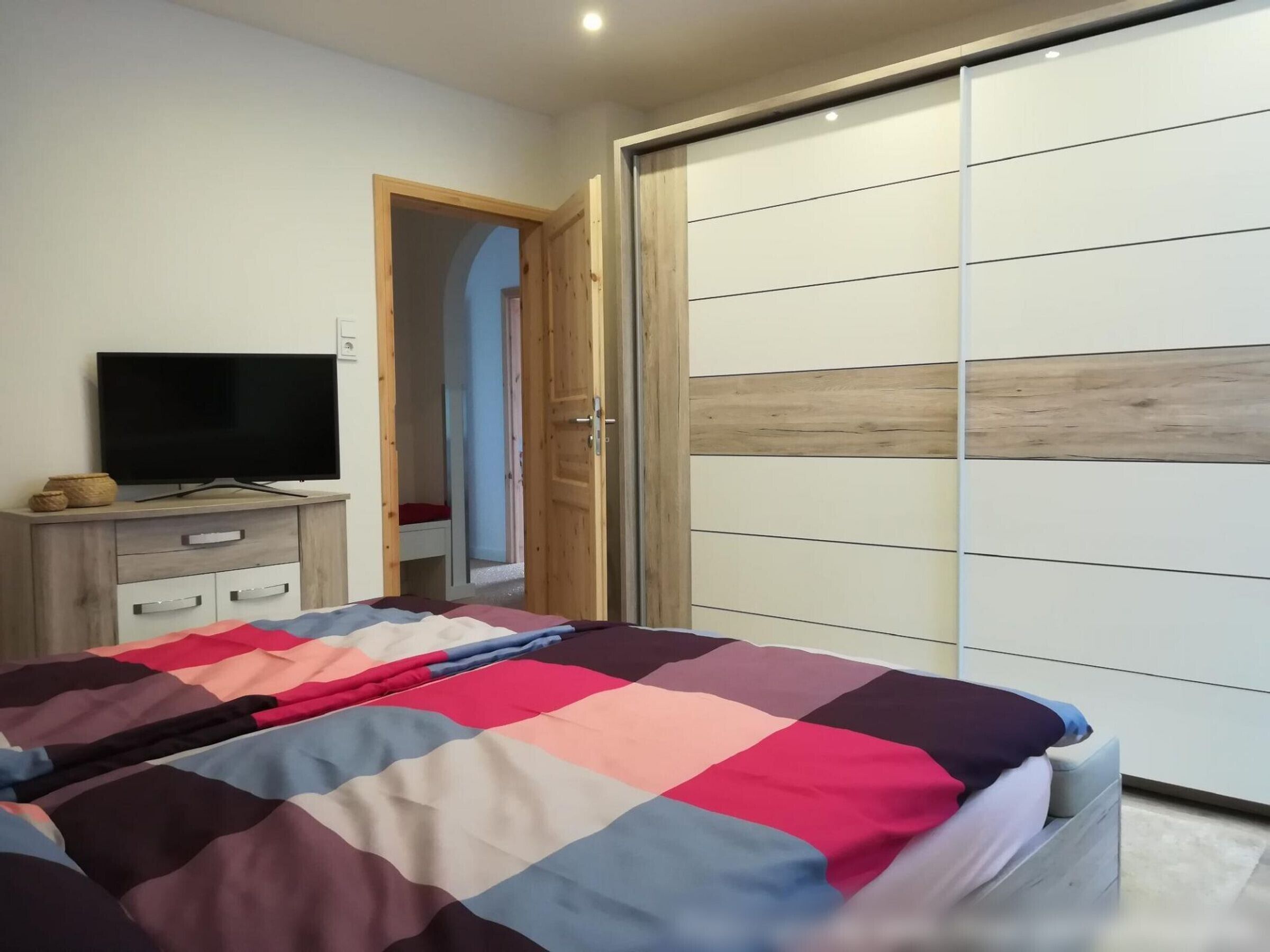 A bedroom with a bed, a TV, a wardrobe, and a door leading to another room.