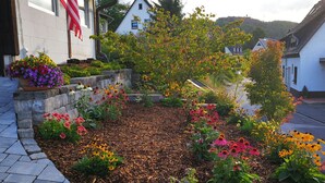 Un jardin aménagé avec une variété de fleurs et d’arbustes, un sentier en pierre et un bâtiment arborant le drapeau américain.