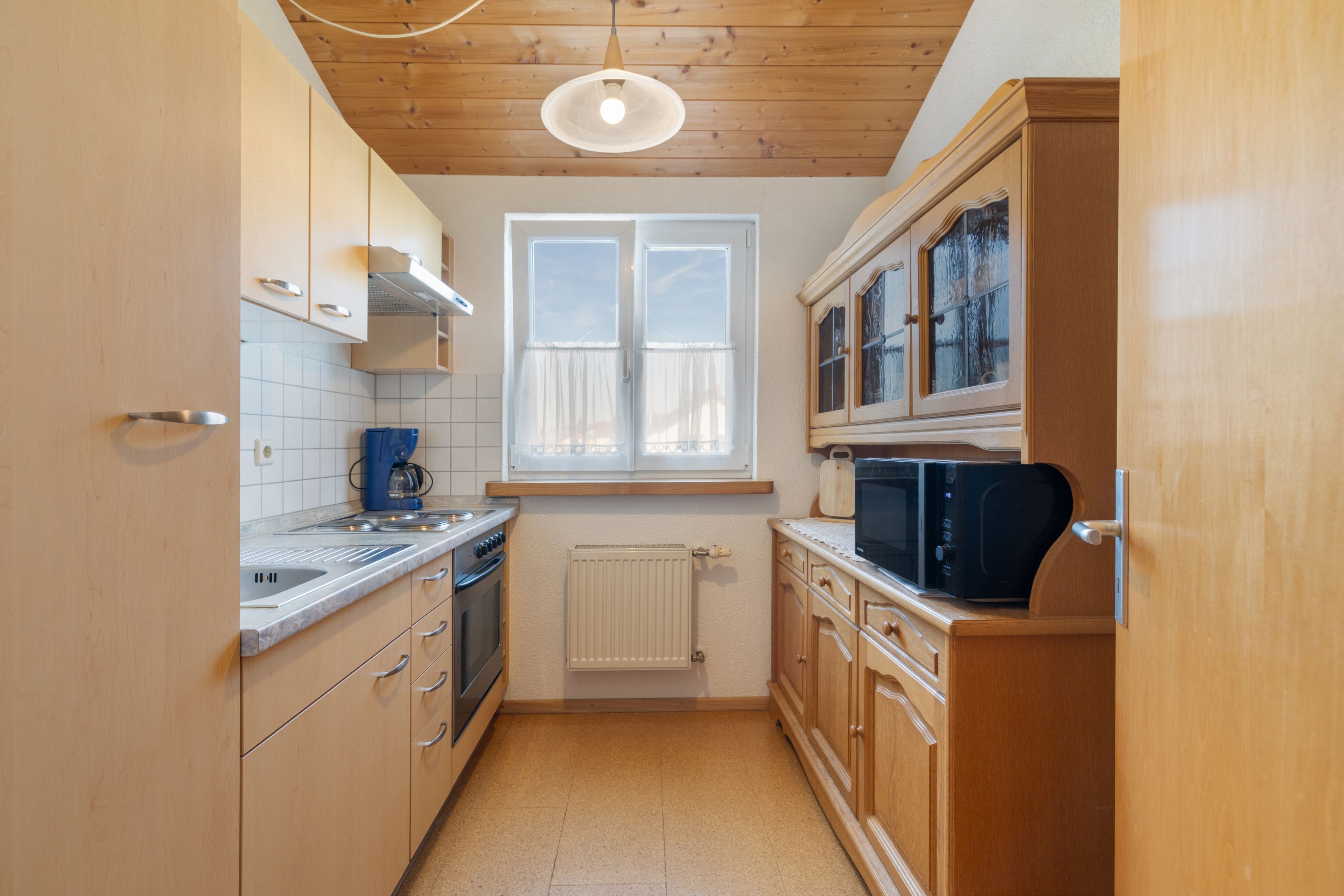 Eine kleine Küche mit Holzausstattung, Backofen, Mikrowelle und einem Fenster über der Spüle.