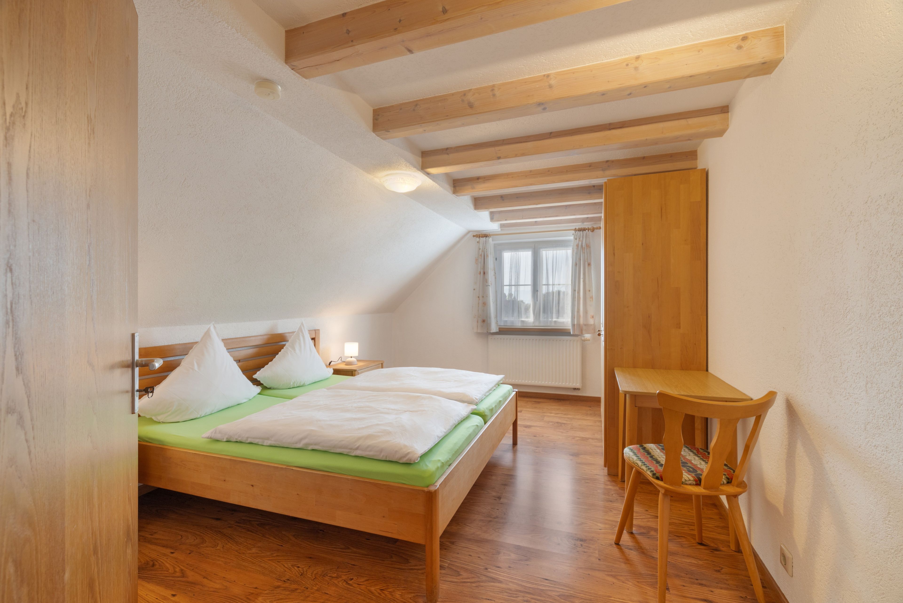 Ein Schlafzimmer mit einem hölzernen Bett, einem Nachttisch, einem Stuhl und einem Fenster mit Vorhängen.