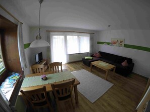Un soggiorno con divano, un tavolo da pranzo con sedie, una televisione e una finestra con tende.