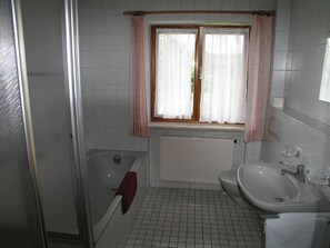 Une salle de bain avec une baignoire, des toilettes, un lavabo et une fenêtre avec des rideaux.
