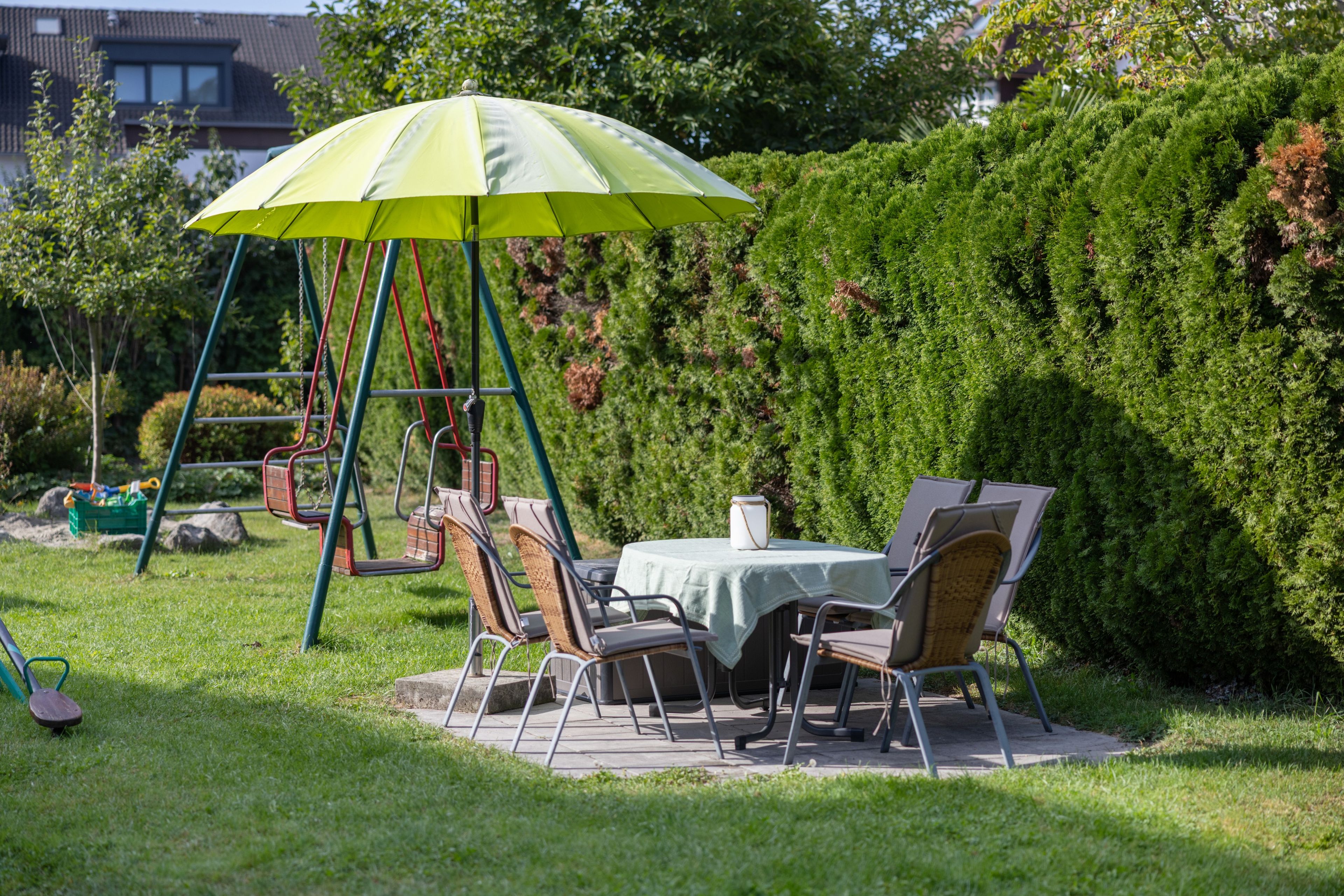 A patio with a swing set, a table with chairs, and a green umbrella.