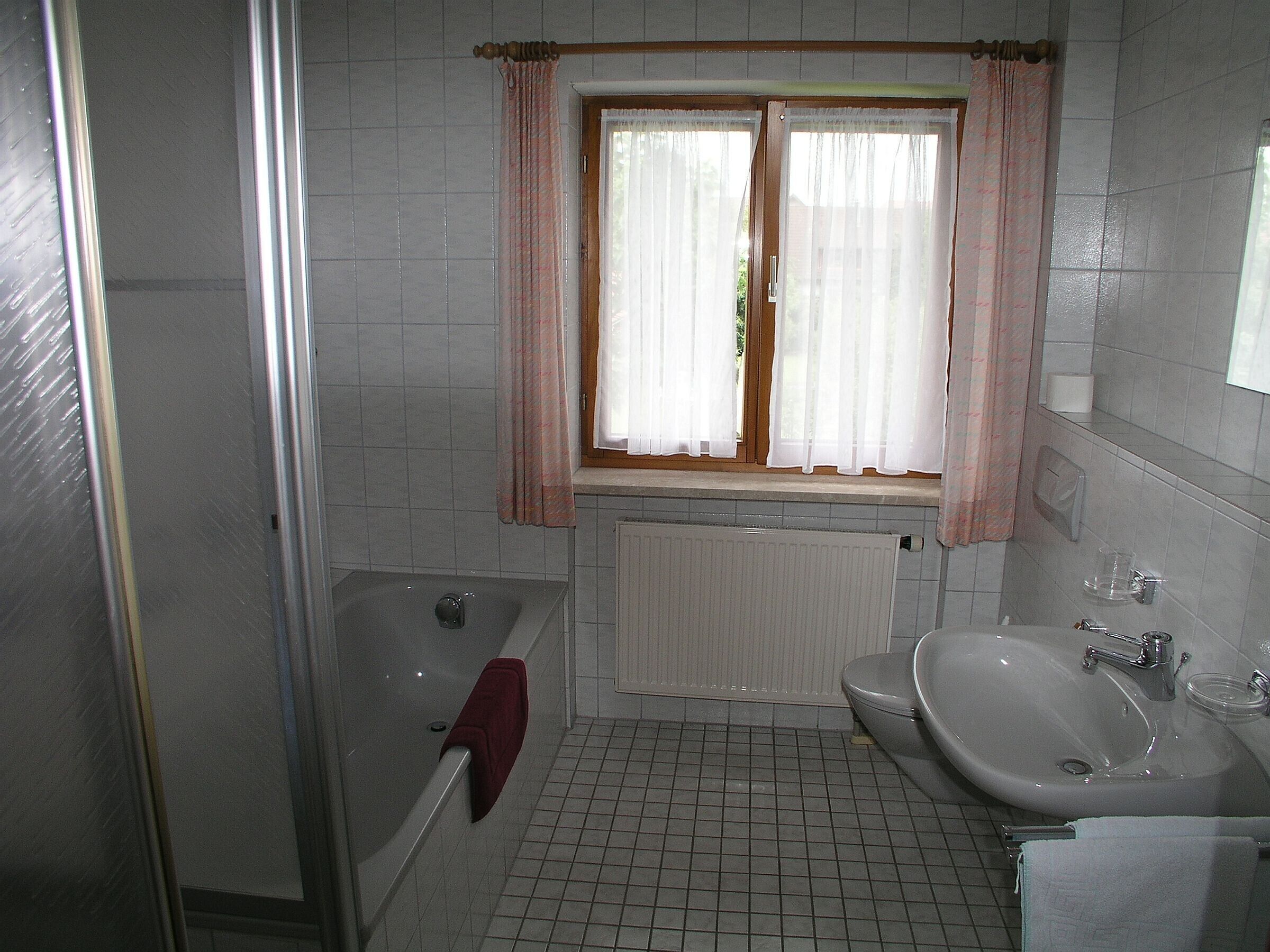 Ein Badezimmer mit einer Badewanne, einer Toilette, einem Waschbecken und einem Fenster mit Vorhängen.