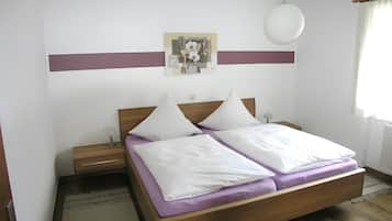 A bedroom with a wooden bed, white pillows, a nightstand, a wall-mounted lamp, and a painting.