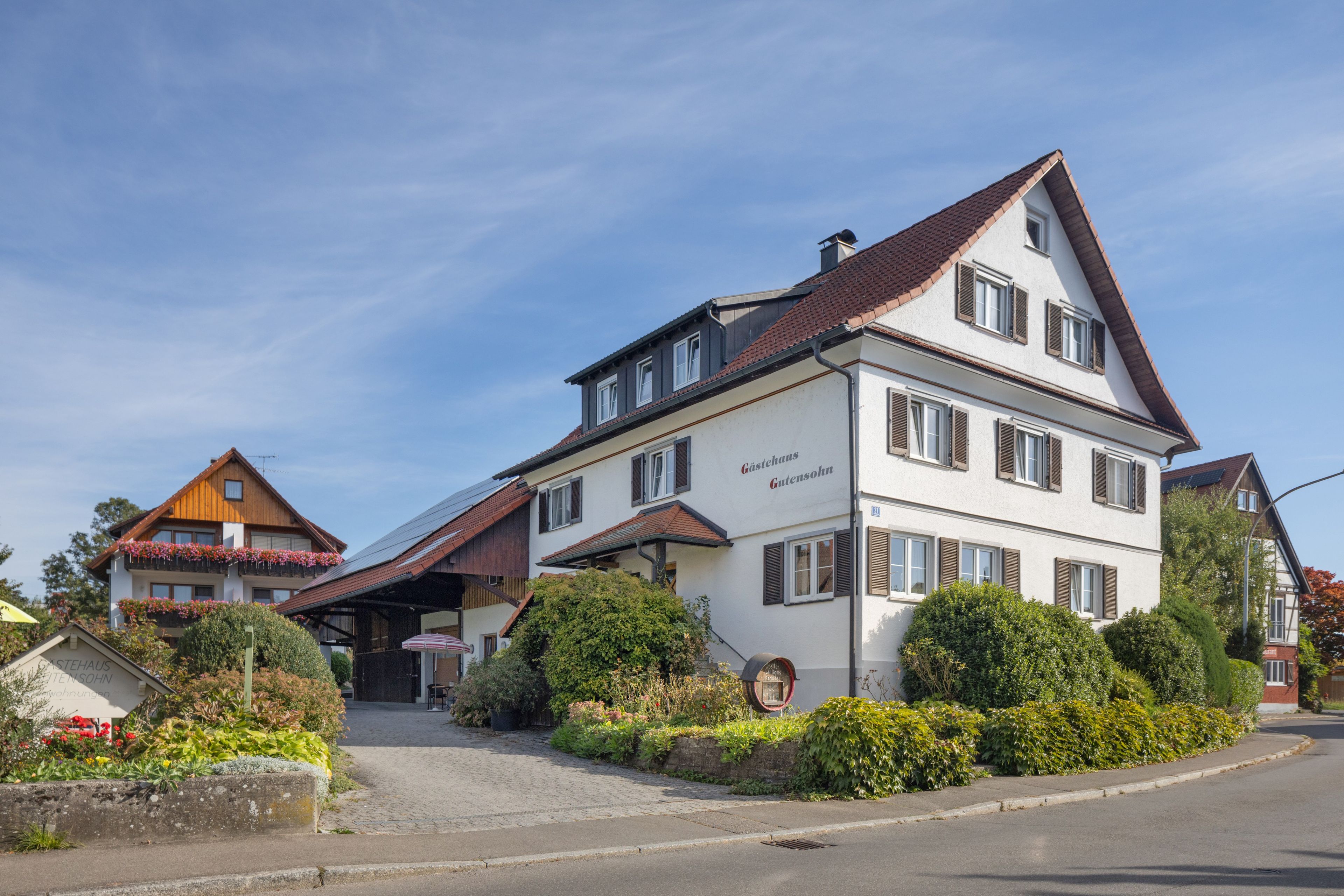 A traditional two-story building with a sloped roof, a sign indicating it is a guesthouse, and a well-maintained garden in front.