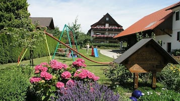 A playground with slides and swings, a sign for Gästehaus Gutensohn, and a building with a red roof.