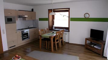 A compact kitchen with a dining area, a television, and a clock on the wall.