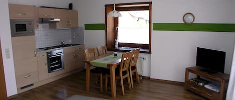 Una cocina compacta con comedor, televisor y un reloj en la pared.