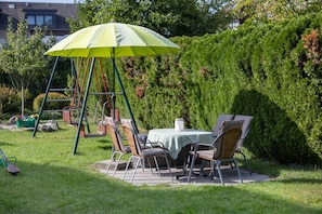 Un patio con un columpio, una mesa con sillas y una sombrilla verde.