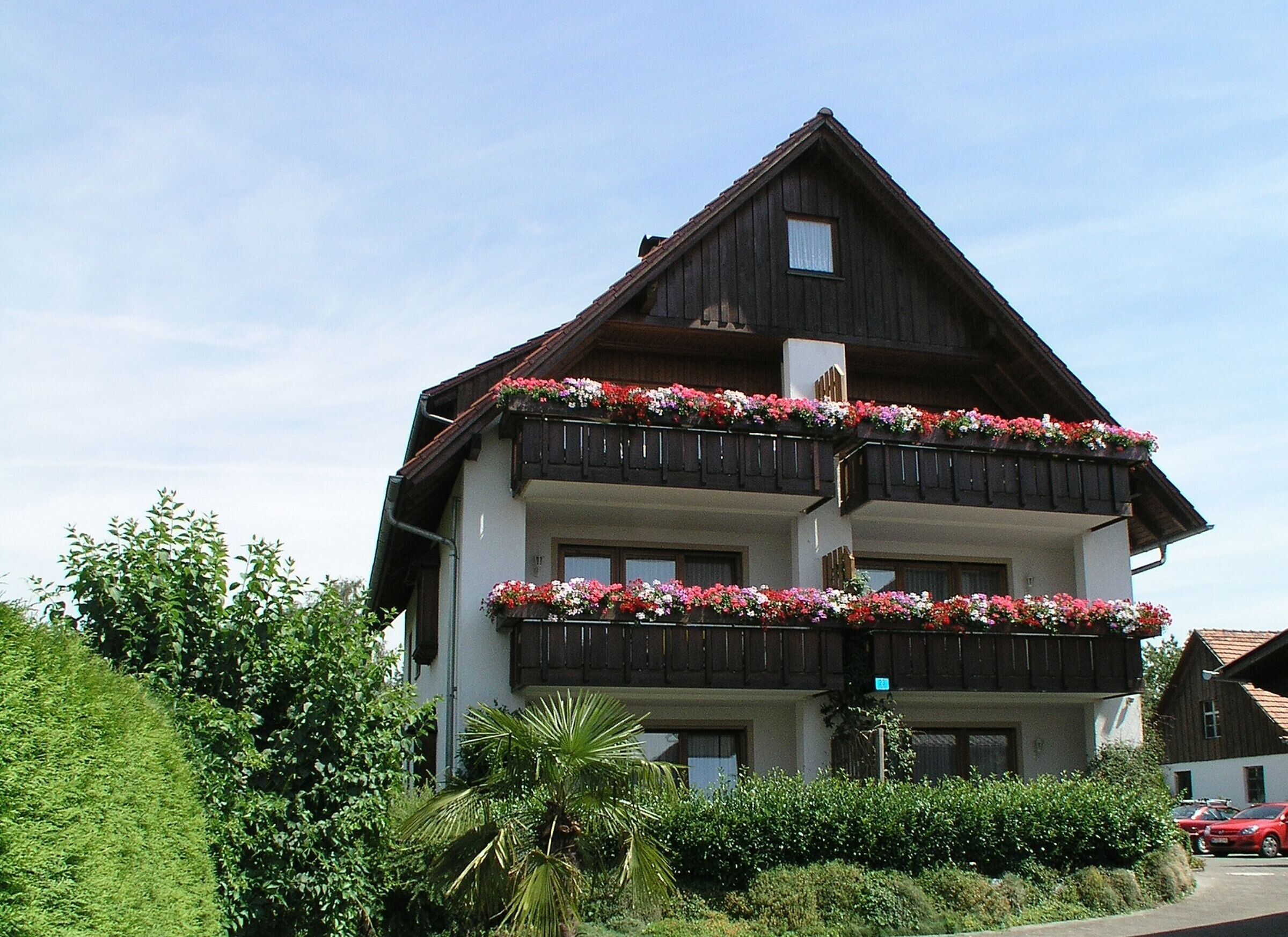Ein mehrgeschossiges Gebäude mit Balkonen, die mit Blumen geschmückt sind, umgeben von Grün.