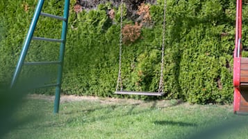Un ginclet amb una escala metàl·lica, un balanceig i una tanca de fullatge al fons.