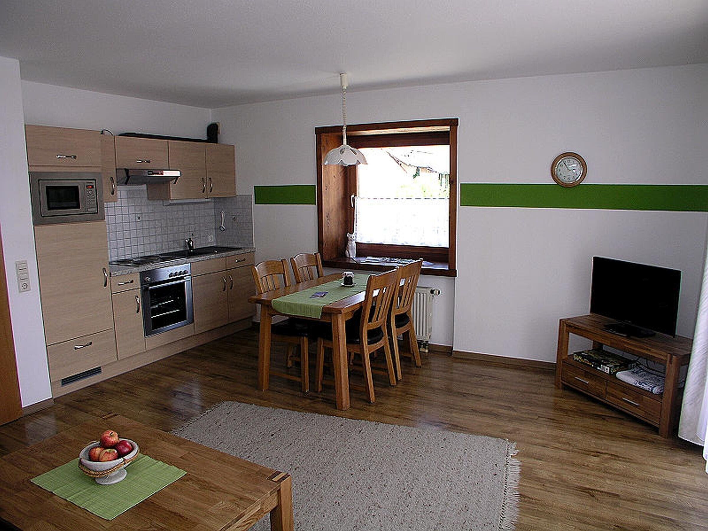 Eine kompakte Küche mit Holzausstattung, einer Mikrowelle, einem Esstisch mit Stühlen, einem kleinen Fernseher und einem Fenster mit Aussicht.