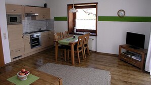 Une cuisine compacte avec des meubles en bois, un four à micro-ondes, une table à manger avec des chaises, une petite télévision et une fenêtre donnant sur un beau paysage.