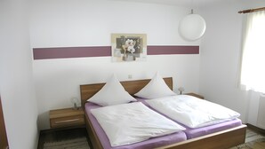 A bedroom with a wooden bed, white pillows, a nightstand, a wall-mounted lamp, and a painting. - Apartment '5' with Shared Terrace, Shared Garden and Wi-Fi (Wasserburg (Bodensee))