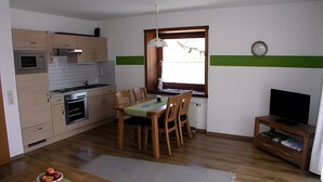 A compact kitchen with a dining area, a television, and a clock on the wall. - Apartment '5' with Shared Terrace, Shared Garden and Wi-Fi (Wasserburg (Bodensee))