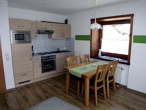 Et kompakt køkken med moderne hårde hvidevarer, et spisebord med stole og et vindue med udsigt.