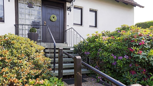 Uma casa com porta escura na frente, um pequeno alpendre e uma escadaria que leva à entrada.