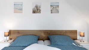 Quarto com cabeceira de madeira, duas mesas de cabeceira com luminárias, cama com roupa de cama estampada e três quadros na parede.