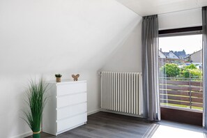 Ein Zimmer mit weißem Schminktisch, einem Heizkörper und Blick auf einen Garten durch ein Fenster.