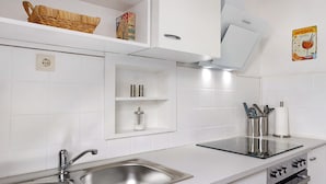Uma cozinha moderna com pia de aço inoxidável, forno embutido e micro-ondas. Há armários brancos e um cesto suspenso na bancada.