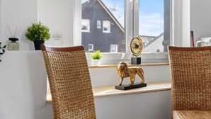 Une pièce avec deux fauteuils en osier, une petite statue de lion doré posée sur une étagère, une plante en pot et une vue sur une maison par la fenêtre.