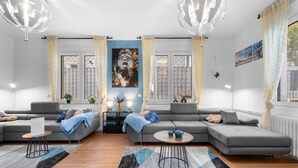 Un salon moderne avec un canapé d’angle gris, une table basse ronde et un grand tableau représentant un lion.