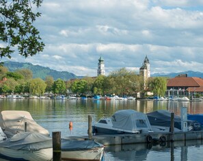 A marina with boats docked, a church with a tower, and a mountain backdrop.