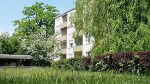 A multi-story residential building with balconies, surrounded by lush greenery and flowering trees.